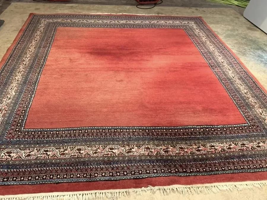 Large patterned rug with an uneven faded red field before professional colour restoration