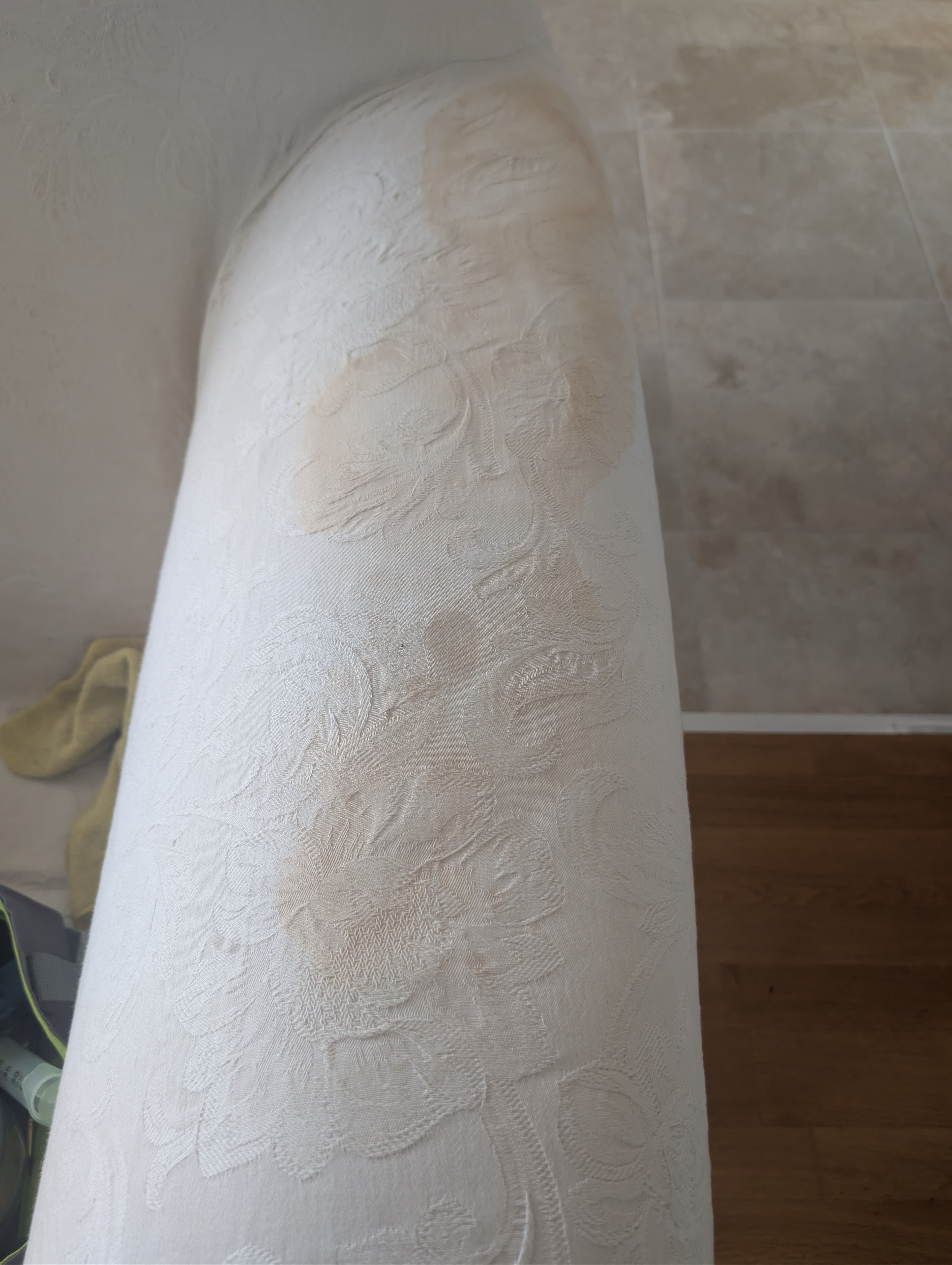 Close view of brown discolouration running along the arm of a white patterned cotton sofa