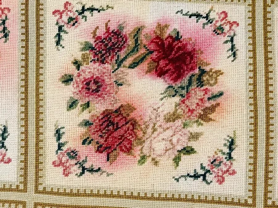 Floral needlepoint rug with pink dye bleed across the pale background before professional correction